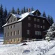 Dřevěná horská chata Skalka ve sněhu mezi smrky